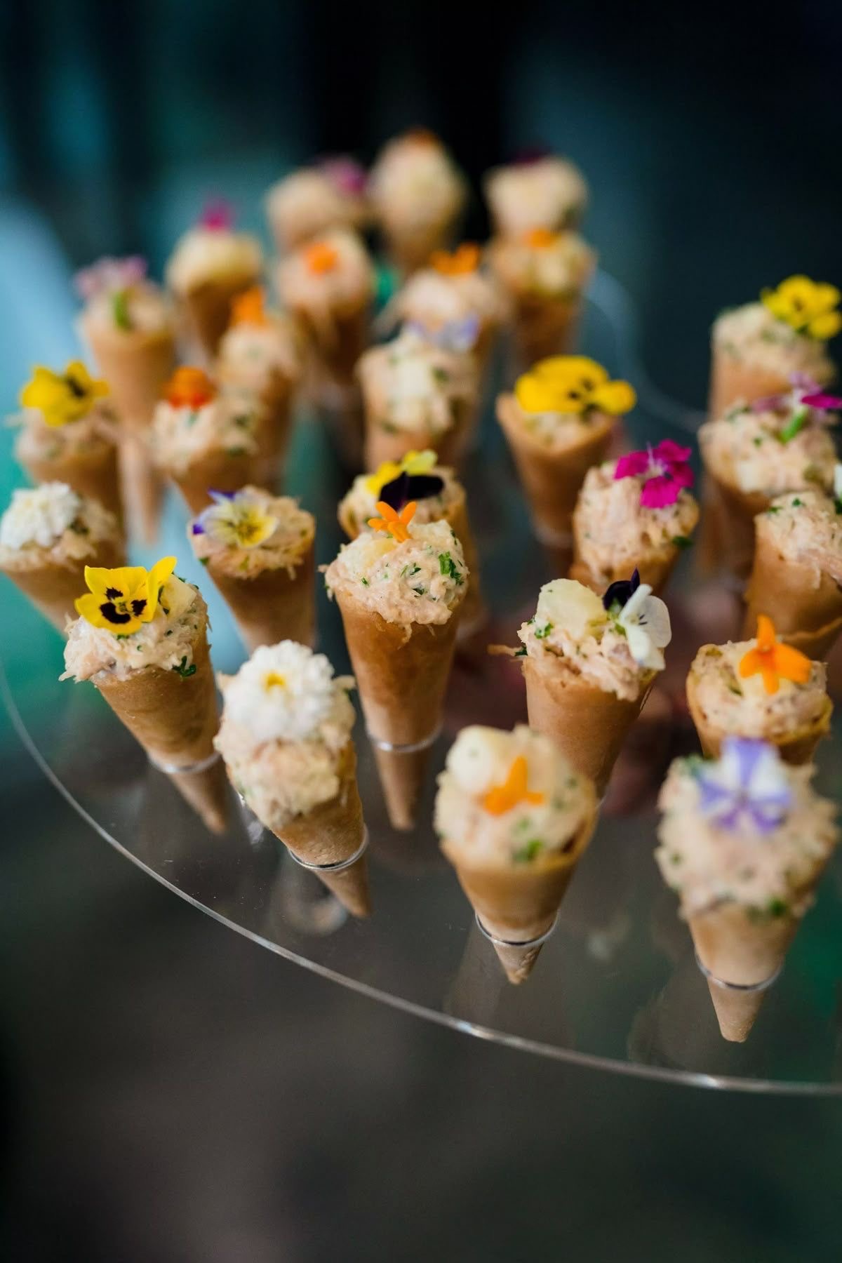 Savoury cones topped with edible flowers arranged on a glass stand at a reception