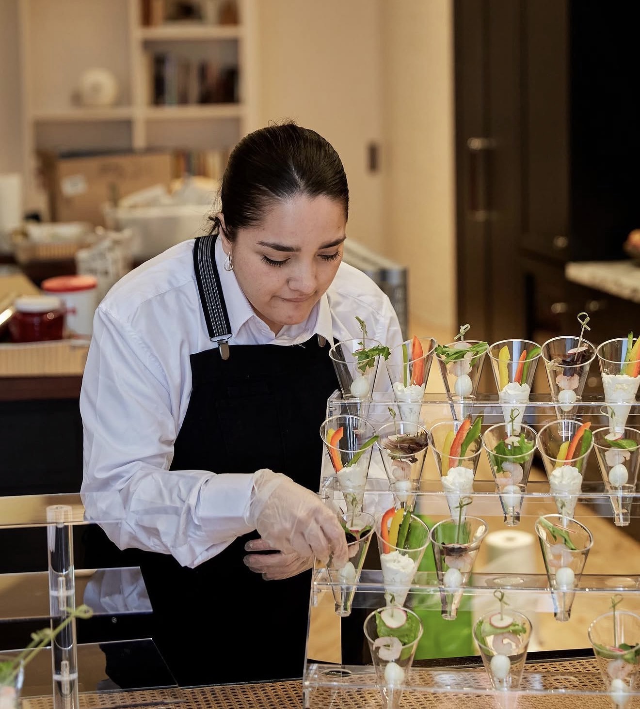 A host carefully arranging elegant small-bite cups in a warm, intimate setting with soft ambient light