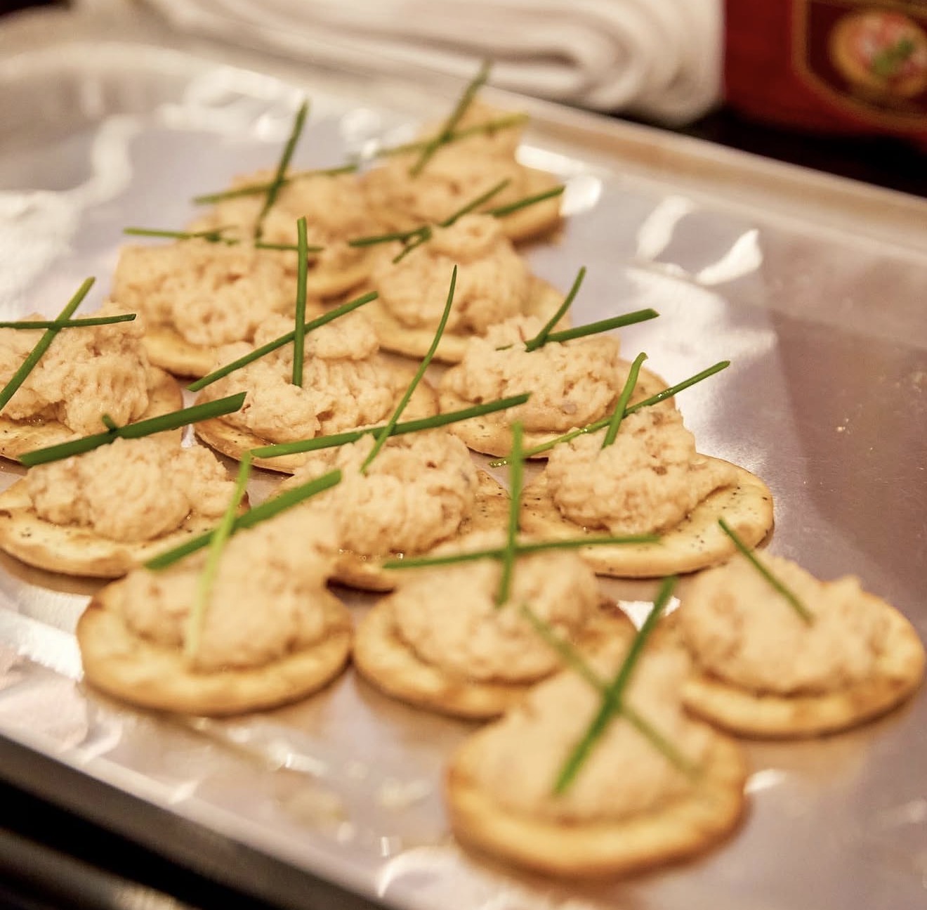 Circular cracker-based canapés topped with salmon mousse and crossed chives arranged on a polished tray
