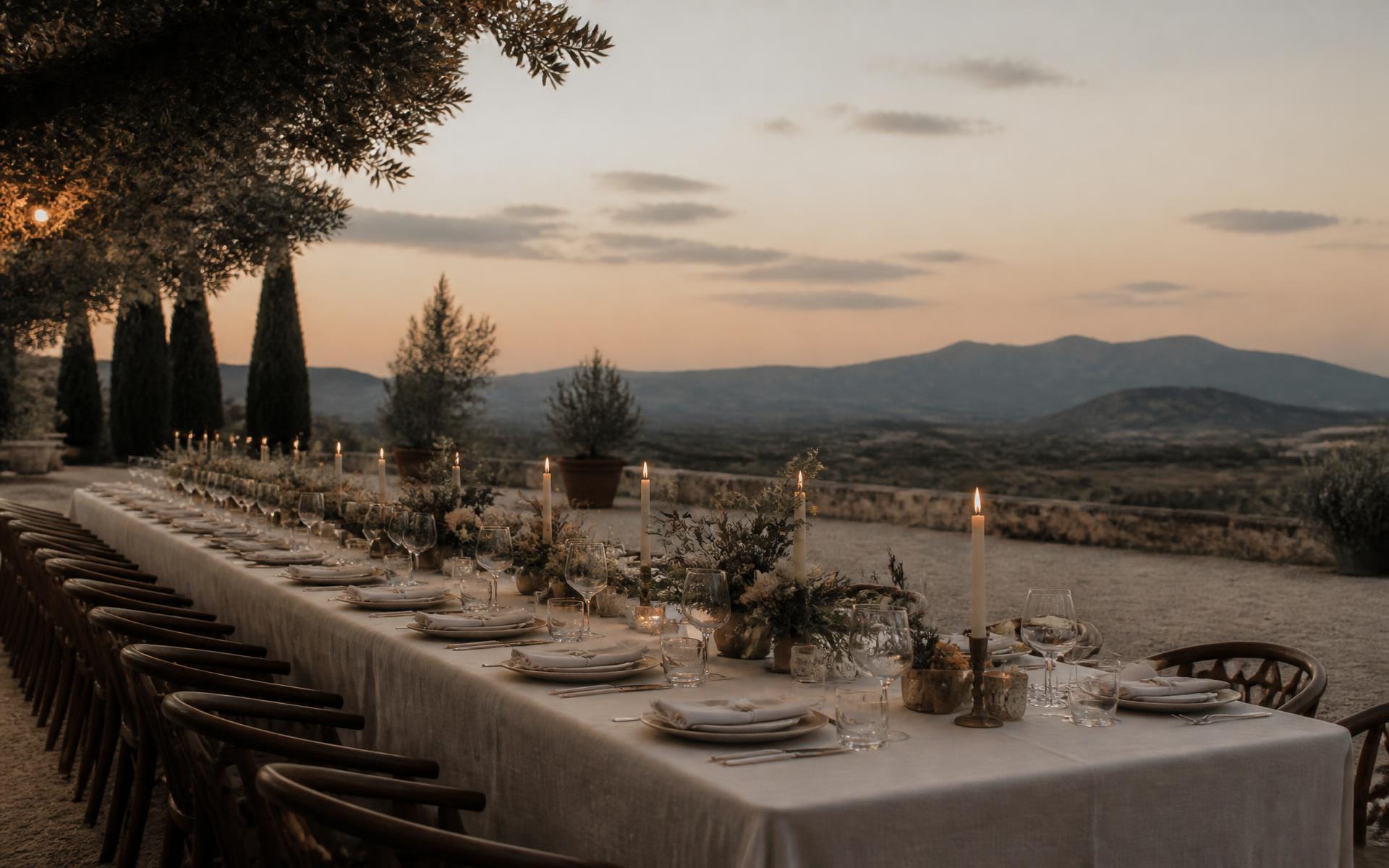 A long linen-dressed table set with candles at dusk